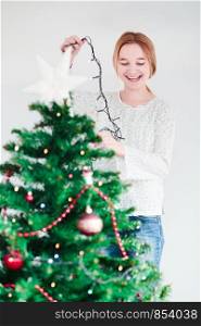 Young girl decorating Christmas tree with lights at home