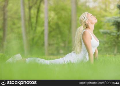 Young girl doing cobra asana yoga exercise in spring park. Young girl doing yoga in park