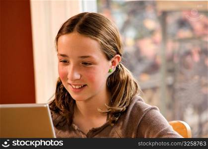 Young girl doing homework on wireless laptop computer at home.