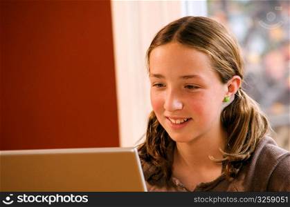 Young girl doing homework on wireless laptop computer at home.
