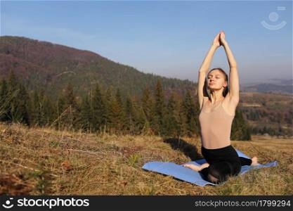 Young girl doing yoga fitness exercise outdoor in beautiful mountains landscape. Morning sunrise, Namaste Lotus pose. Meditation and Relax. Healthy Lifestyle. Young girl doing yoga fitness exercise outdoor in beautiful mountains landscape. Morning sunrise, Namaste Lotus pose. Meditation and Relax. Healthy Lifestyle.