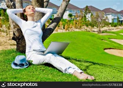 Young girl dressed in white rest lying on a tree with her laptop.