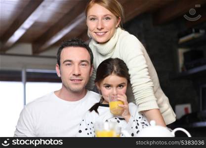 Young girl drinking a glass of orange juice while posing for the camera with her parents