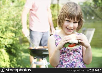 Young Girl Eating Beefburger At Family Barbeque