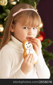 Young Girl Eating Cookie In Front Of Christmas Tree