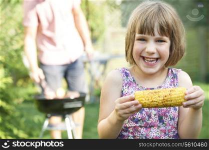 Young Girl Eating Sweetcorn At Family Barbeque