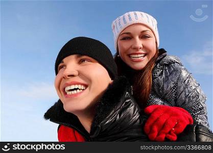 young girl embracing man from back, smiling and looking at camera, sky on background