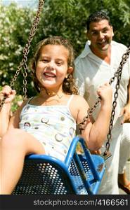 Young girl enjoying swing ride with father in background