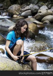 Young girl focused on fishing in remote stream with rocks and swift water in background
