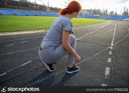 young girl getting ready for a run through the stadium and tying shoelaces on sports shoes. girl tying shoelaces