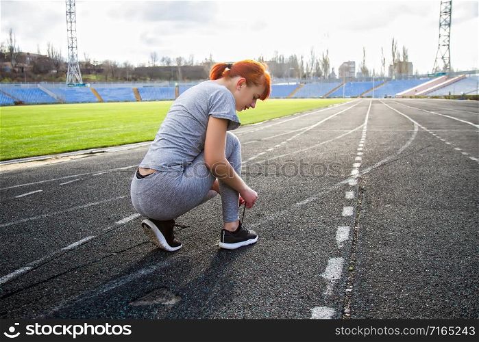 young girl getting ready for a run through the stadium and tying shoelaces on sports shoes. girl tying shoelaces