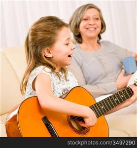 Young girl granddaughter sing play guitar to grandmother smile