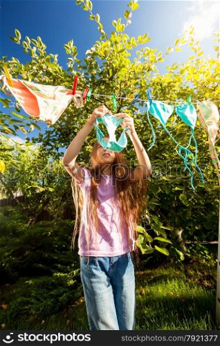 Young girl hanging clothes with clothespins at sunny day