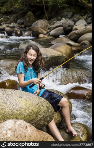 Young girl having fun fishing barefoot on stream in woods during summer