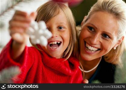 Young girl helping her mother decorating the Christmas tree, holding some Christmas decoration in her hand (Focus on girl)