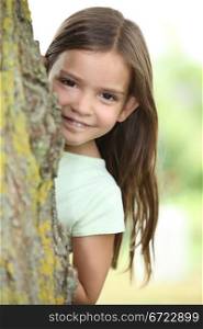 Young girl hiding behind a tree