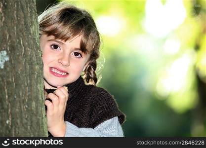 Young girl hiding behind a tree trunk