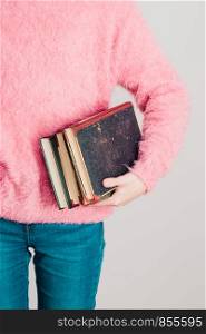 Young girl holding a few books. Teenager girl wearing pink sweater and blue jeans. Vertical photo
