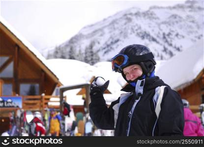 Young girl holding a snowball in front a chalet at downhill ski resort