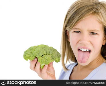 Young girl holding broccoli and sticking tongue out