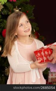 Young Girl Holding Christmas Present In Front Of Christmas Tree