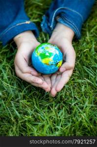 Young girl holding Earth in hands against green grass