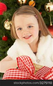 Young Girl Holding Gift In Front Of Christmas Tree