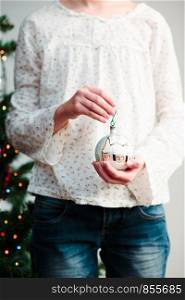 Young girl holding hand painted ball decorating Christmas tree at home