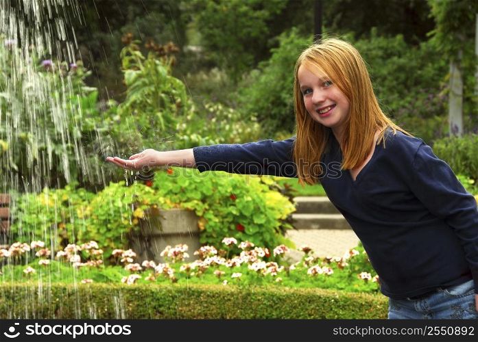 Young girl holding her hand under falling water in a garden