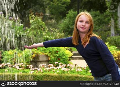 Young girl holding her hand under falling water in a garden