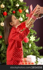 Young Girl Holding Wrapped Present In Front Of Christmas Tree