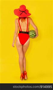 young girl in a bright red swimsuit and a wide-brimmed red hat eats a watermelon on a yellow background. girl with watermelon