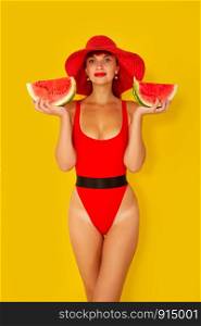 young girl in a bright red swimsuit and a wide-brimmed red hat eats a watermelon on a yellow background. girl with watermelon