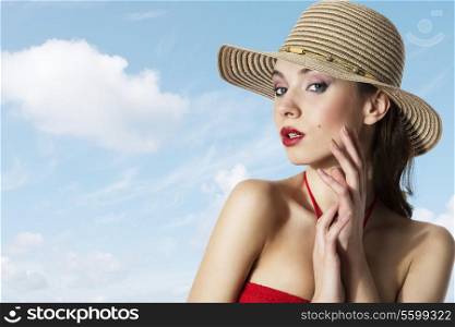 Young girl in a hat is holding her hand near face , and wearing a summer hat on blue light sky