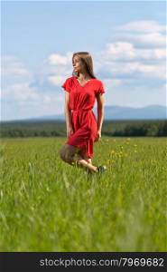 Young girl in a red dress on lawn with blue sky with clouds