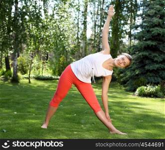 Young girl in a white shirt and red pants doing yoga outdoors