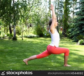 Young girl in a white shirt and red pants doing yoga outdoors