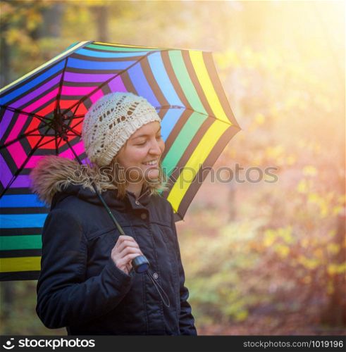 Young girl in blue coat and umbrella is taking a walk through the autumnal forest