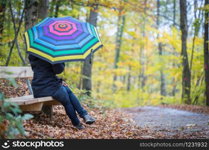 Young girl in blue coat and umbrella is taking a walk through the autumnal forest