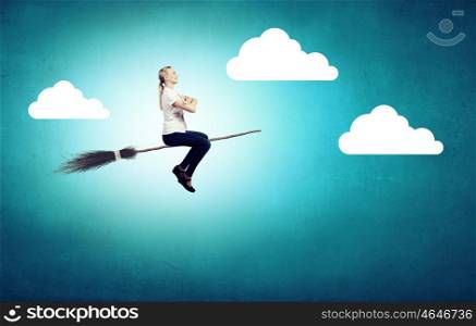 Young girl in casual flying on broom high in sky. Girl on broom
