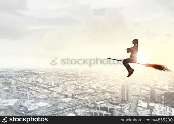 Young girl in casual flying on broom high in sky. Girl on broom