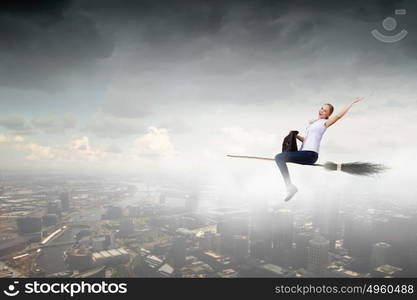 Young girl in casual flying on broom high in sky. Girl on broom