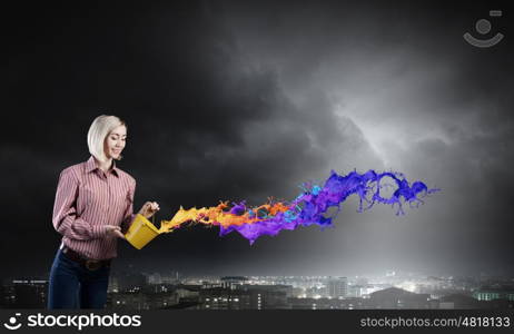 Young girl in casual splashing colorful paint from bucket