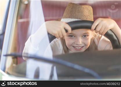 Young girl in driving seat of car, holding steering wheel, smiling