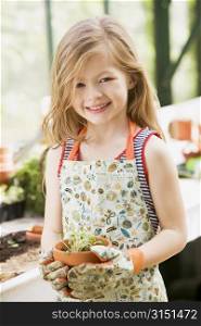 Young girl in greenhouse holding potted plant smiling