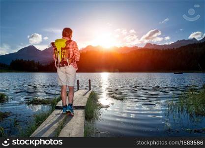 Young girl in hike on the small pier of an alpine lake in the summer