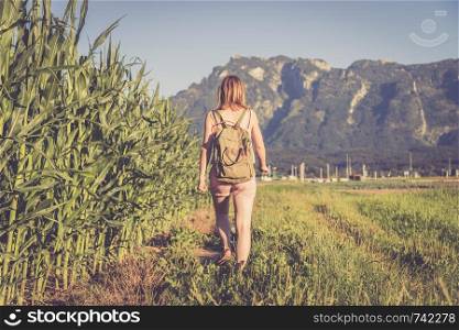 Young girl in jumpsuit with backpack is taking a walk on a field, summer time
