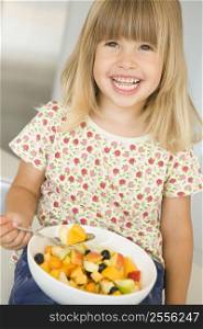 Young girl in kitchen eating bowl of fruit smiling