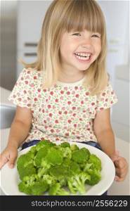 Young girl in kitchen eating broccoli smiling