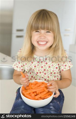 Young girl in kitchen eating carrot sticks smiling